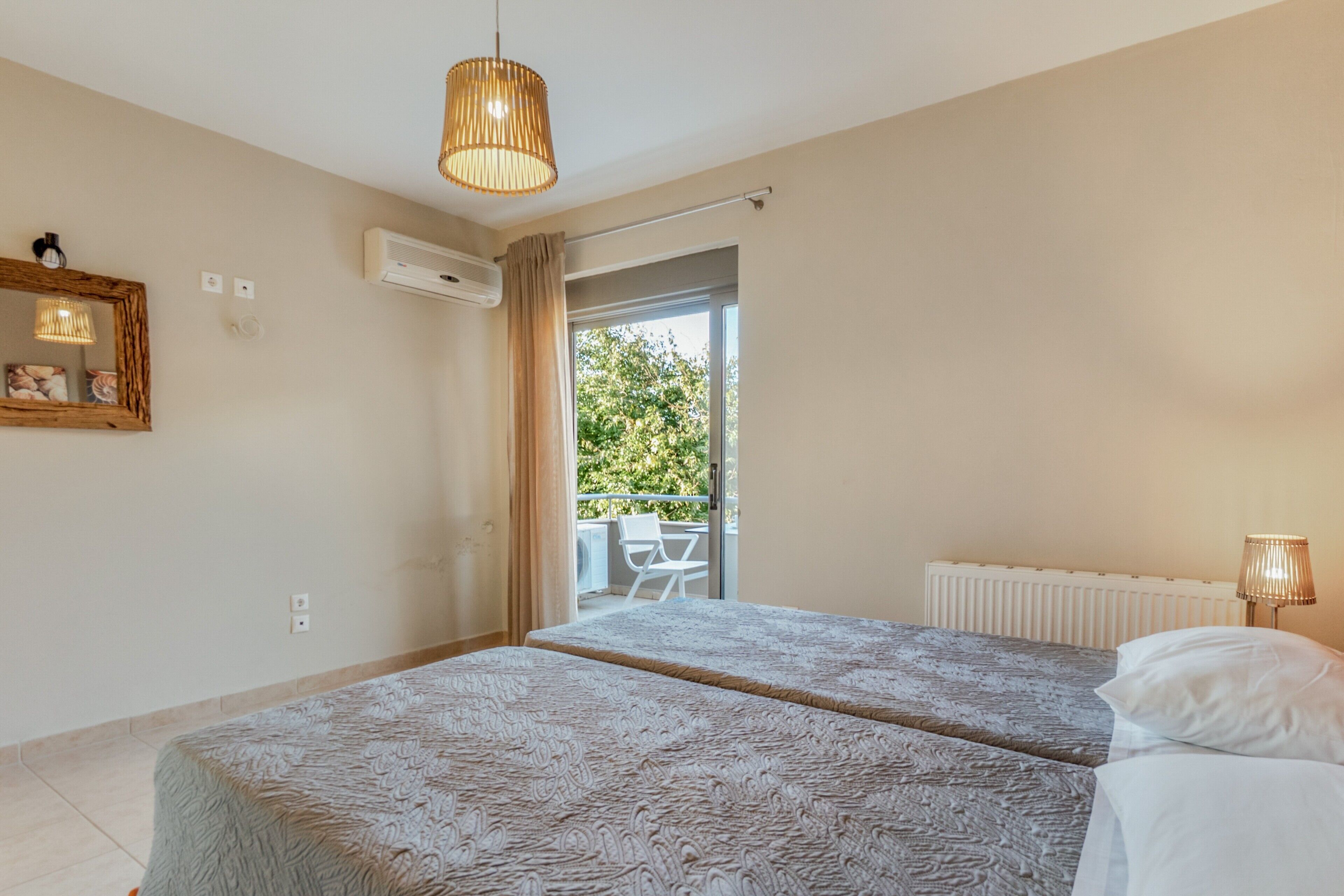 A bedroom with two beds, a window, an air conditioning unit, a ceiling light, and a view of the outdoors.