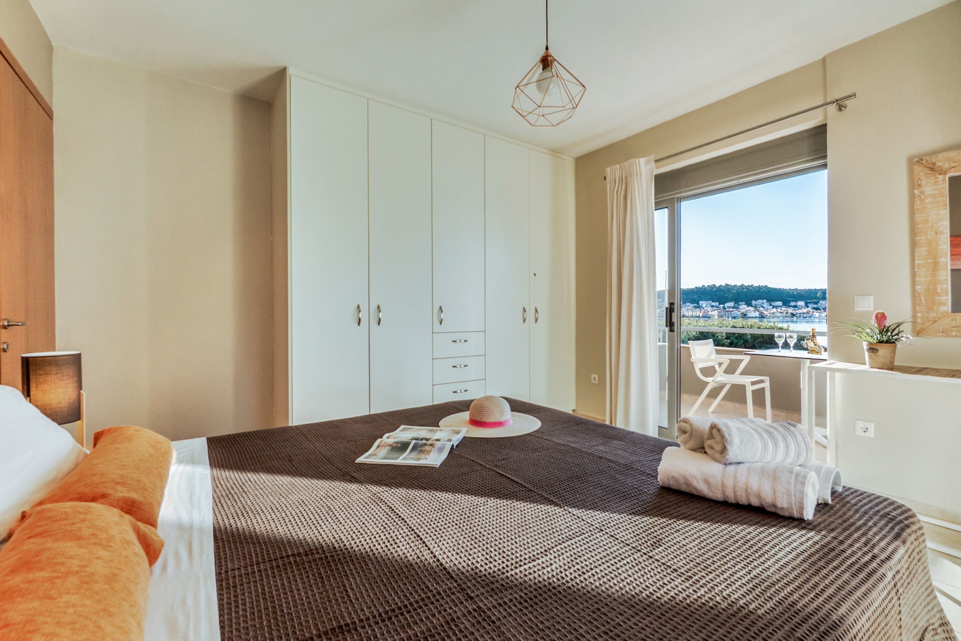 A hotel room with a bed, a wardrobe, a desk, and a view of the city.