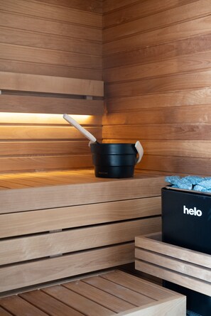 Een sauna met houten wanden en banken, een zwarte emmer en een zwarte tas met de tekst 'helo'.