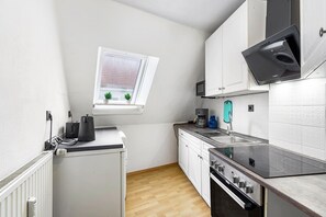 Cozinha compacta com janela, armários brancos, forno embutido e bancada com chaleira e cafeteira.