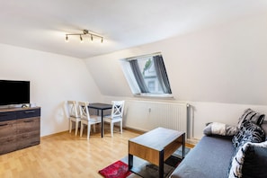 Uma sala de estar moderna com televisão, mesa de jantar, cadeiras, sofá e uma janela com cortinas.