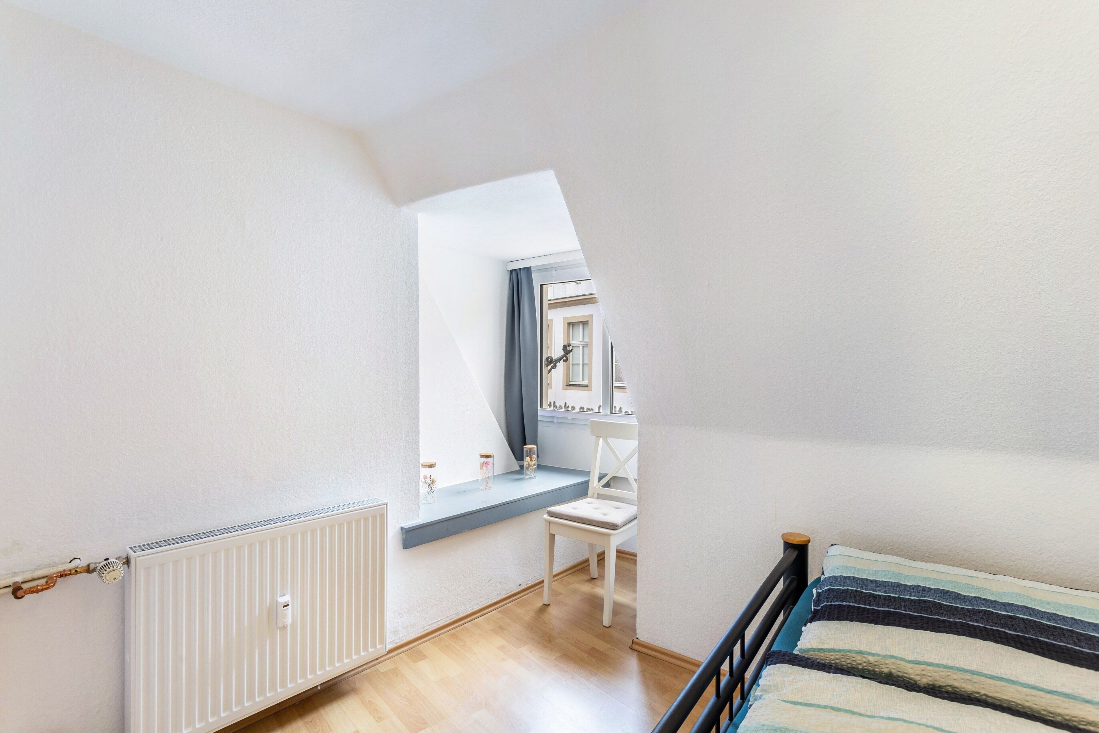Ein Zimmer mit Fenster, Heizkörper, Stuhl und Bett.