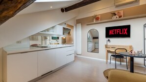 Una cocina moderna con armarios blancos, un comedor con mesa y sillas, y un televisor montado en la pared mostrando 'NETFLIX'.