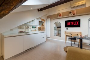 A modern kitchen with white cabinets, a dining area with a table and chairs, and a wall-mounted TV displaying 'NETFLIX'.