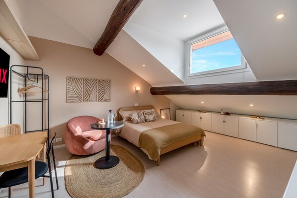 A bedroom with a loft-style ceiling, a bed, a small round table, a chair, and a wardrobe.