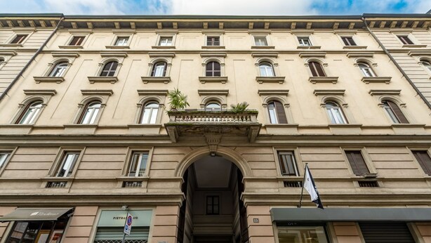 Un edificio de varios pisos con entrada central, ventanas grandes y un balcón con plantas.