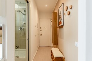 A hallway with a glass shower enclosure, a bench, and a door with a wooden panel.