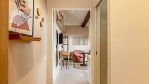 Un pasillo que conduce a una habitación con una cama, una silla, una mesa y una pared con un diseño geométrico.