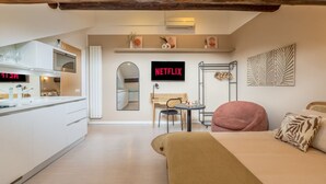 Una cocina moderna con horno empotrado, un comedor con mesa y sillas, una cama con cabecera y un letrero de Netflix sujeto a la pared.