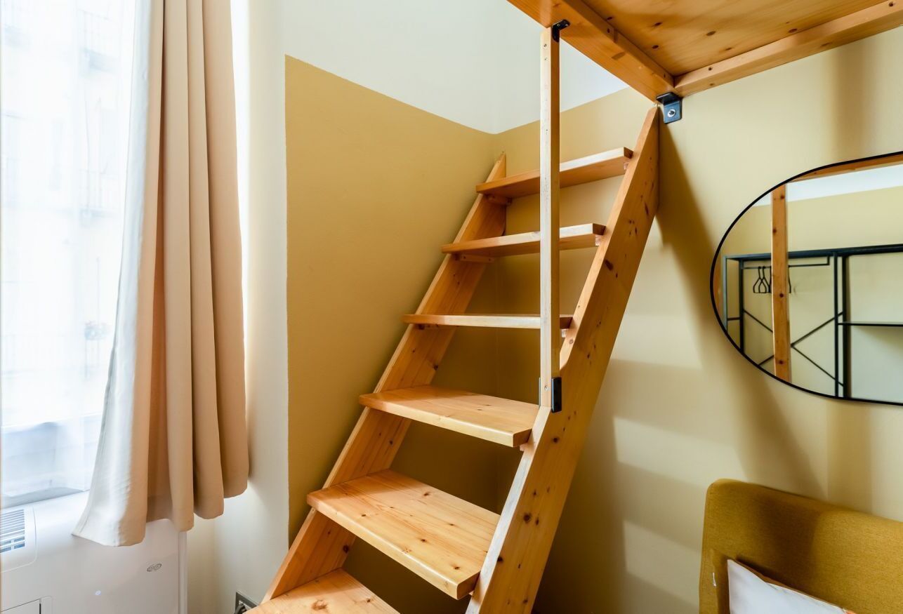 Un escalier en bois avec une rampe métallique, une fenêtre avec des rideaux et un miroir rond accroché au mur.