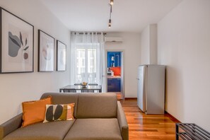 A modern living room with a sofa, a dining table, and a kitchen area in the background.