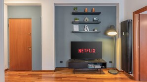 Een woonkamer met een flatscreen-tv waarop 'NETFLIX' staat, een houten deur en een radiator.