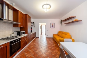 A kitchen with wooden cabinets, a gas stove, and a microwave. There is a yellow sofa and a white table in the living area.