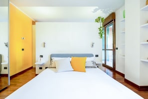 A modern bedroom with a large bed, bedside tables, a mirror, and a window with blinds.