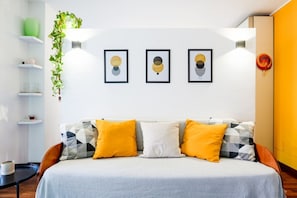 A modern bedroom with a bed, a wall-mounted shelf with decorative items, and framed artwork.