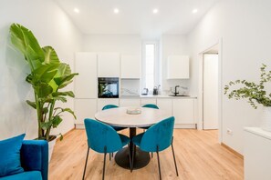 A modern kitchen with white cabinets, a round dining table with blue chairs, and a large plant.