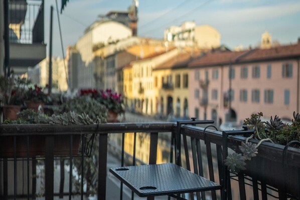 A balcony with a metal table and chairs, potted plants, and a view of buildings with domed and traditional architecture.