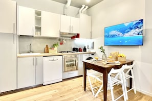 Uma cozinha moderna com armários brancos, bancada de madeira, mesa de jantar com cadeiras e uma TV na parede.