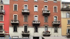 Ein mehrstöckiges Gebäude mit Balkonen, einem Schild mit der Aufschrift 'maccheroni' und einer sichtbaren Schaufensterfront.