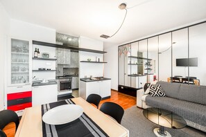 A modern kitchen with white cabinets, a dining area with a table and chairs, and a living area with a sofa and TV.