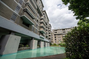 A multi-story residential building with balconies, a swimming pool, and a covered walkway.