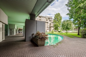 A covered outdoor area with a pool, a planter with shrubs, and a view of residential buildings.
