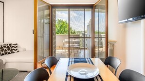Un salon moderne comprenant un canapé, une table à manger avec des chaises, un téléviseur fixé au mur et une porte-fenêtre coulissante donnant sur une terrasse extérieure.