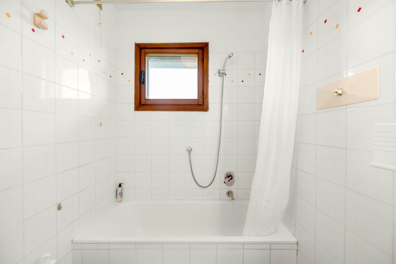 A bathroom with white tiled walls, a shower, a bathtub, a window, and a towel rack.