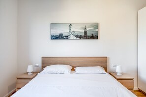 Une chambre d’hôtel avec un lit, deux tables de chevet et un tableau représentant un paysage urbain accroché au mur.