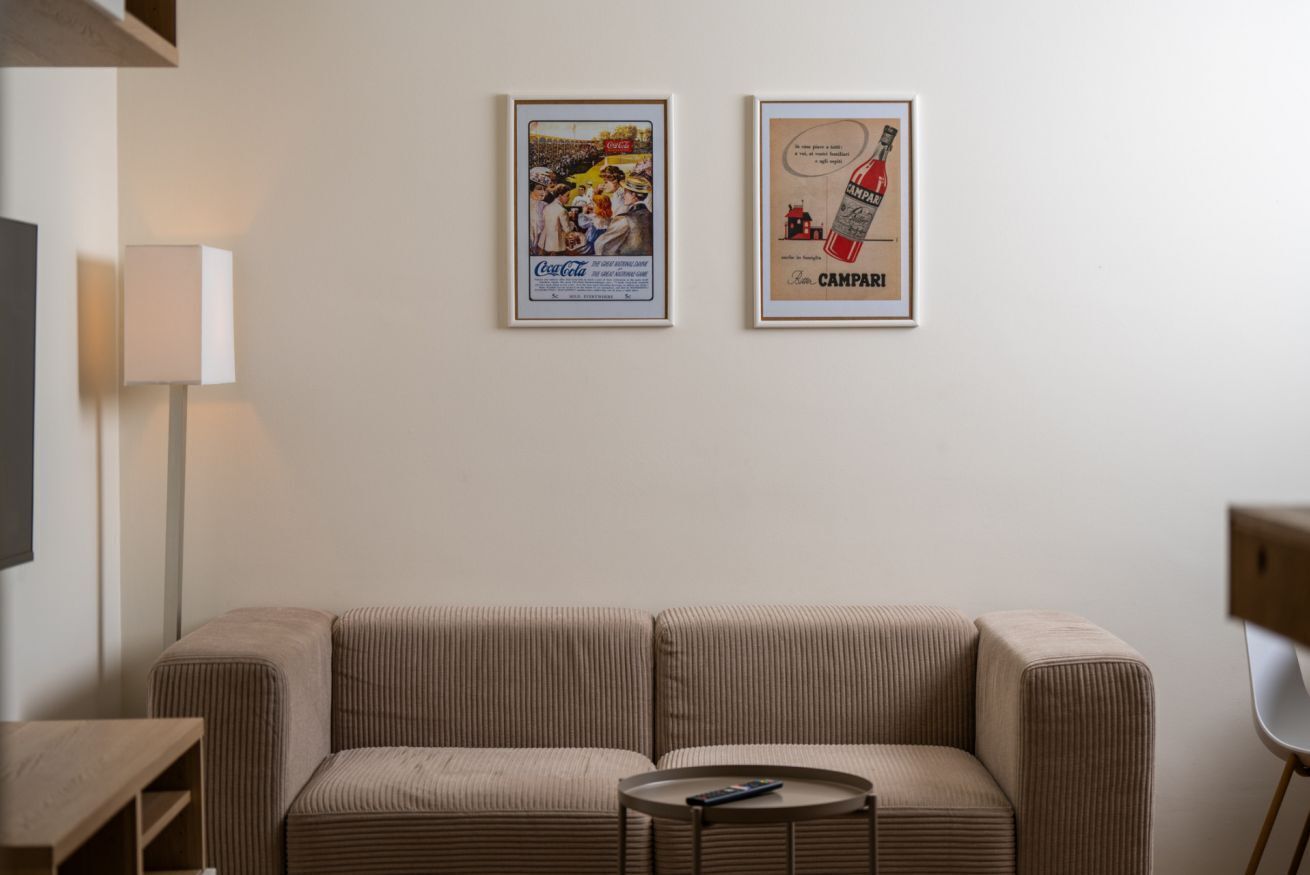 Una sala de estar con un sofá, una mesita redonda y dos carteles enmarcados en la pared.