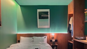 A neatly made bed with white linens, a framed picture on the wall, a bedside lamp, and a wooden nightstand with a small speaker. - kukjejang hotel (Busan)