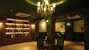 A warmly lit room with a wooden bookshelf, two upholstered chairs, a small round table, and a chandelier. - kukjejang hotel (Busan)