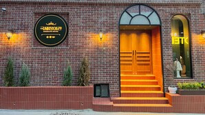 A brick building with a sign for the KURJEJANG HOTEL. There are steps leading to a wooden door with a glass panel above. - kukjejang hotel (Busan)