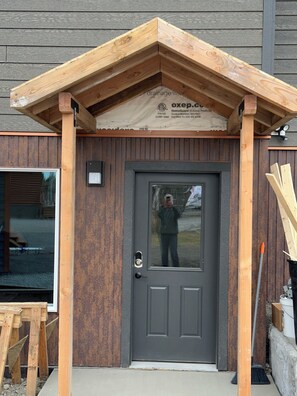 A wooden building with a grey door, a small window, and a sign above the door.