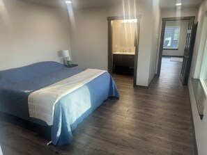 Ein Schlafzimmer mit einem Bett, einem Nachttisch, einer Lampe und einem durch eine offene Tür einsehbaren Badezimmer.