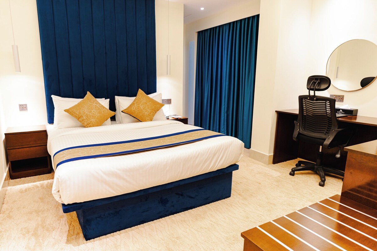 A hotel room with a large bed, a desk, a chair, and a mirror.