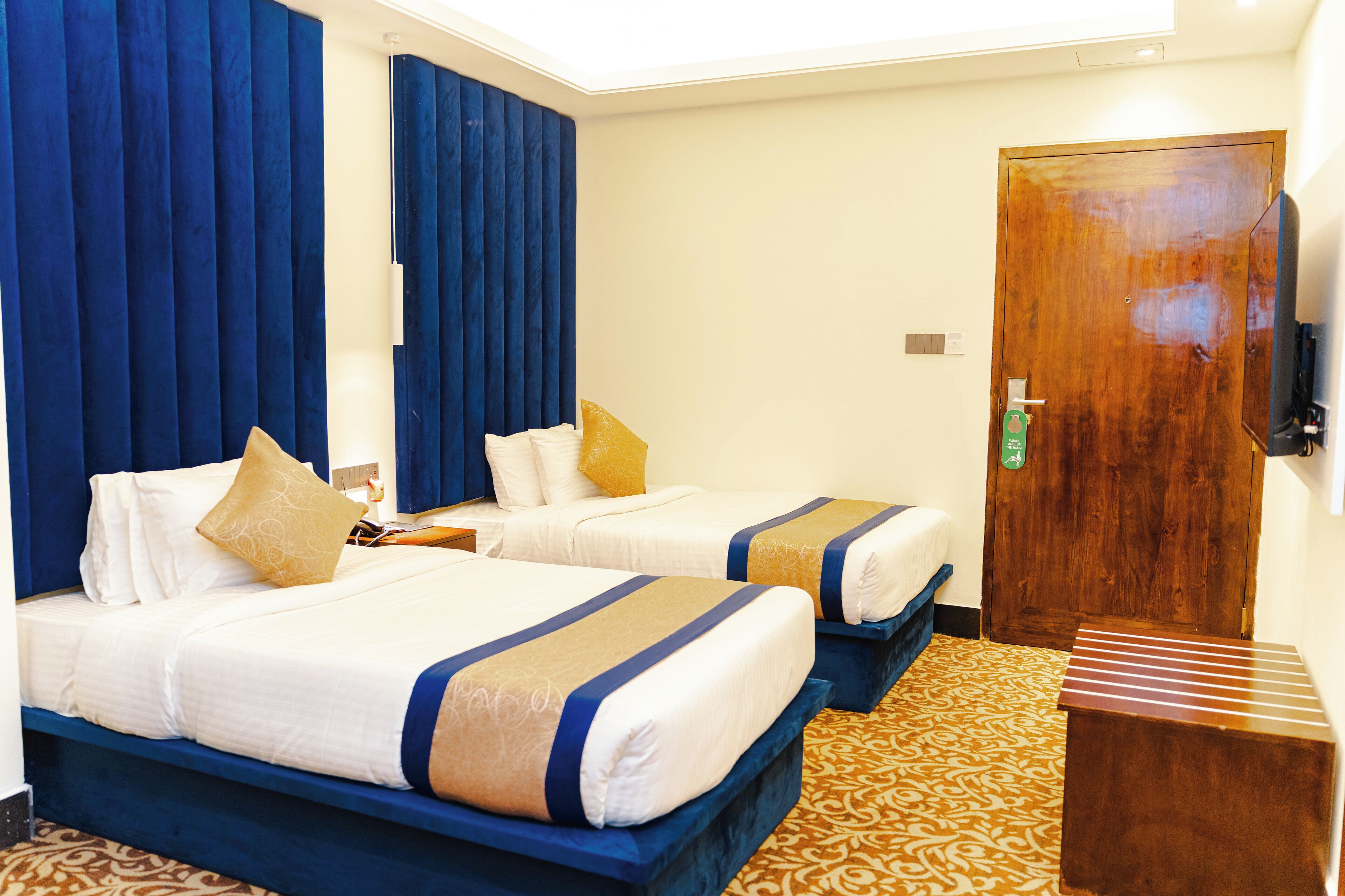 Habitación de hotel con dos camas, una puerta de madera y una alfombra estampada.
