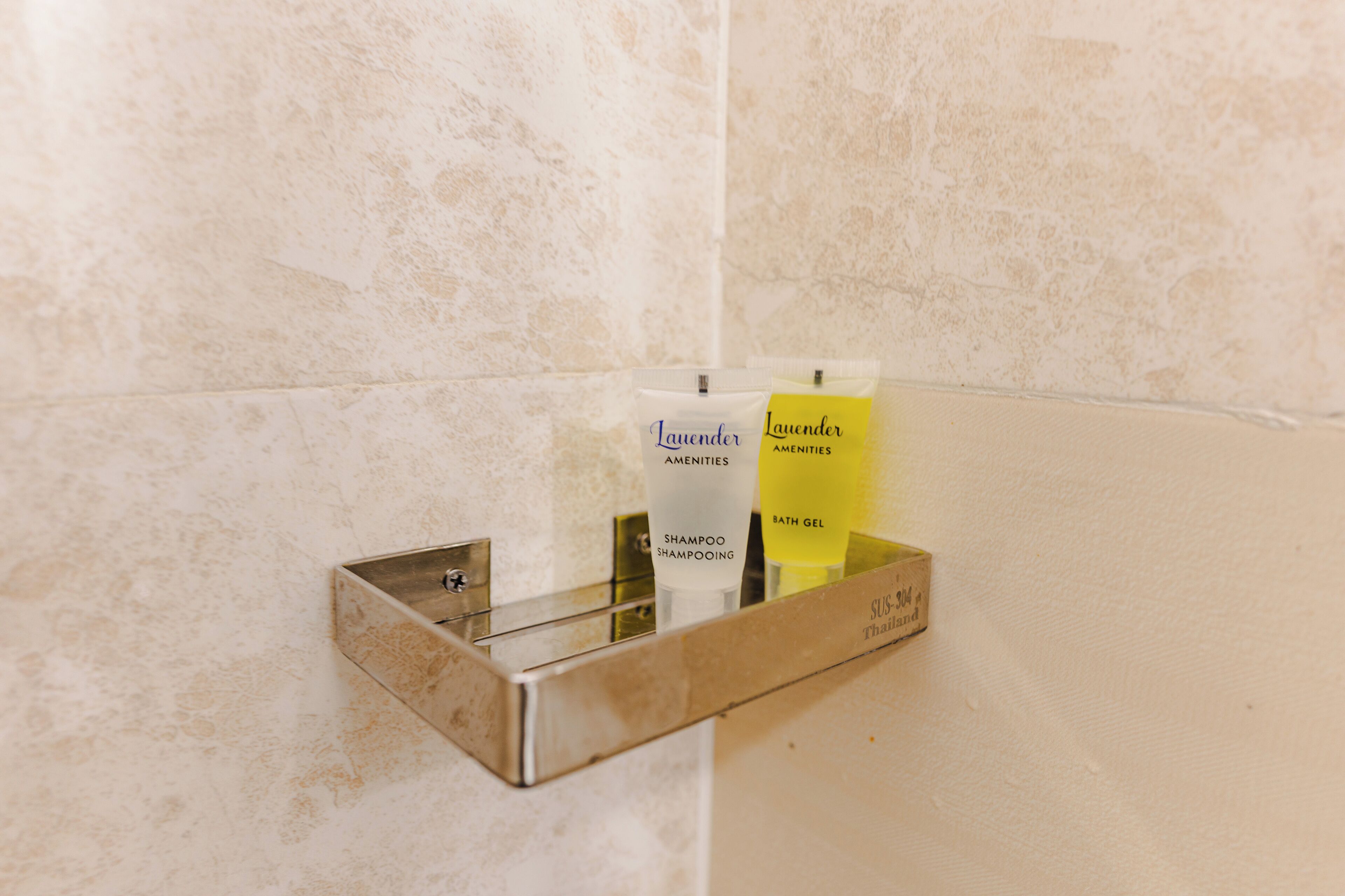 A bathroom with a metal shelf holding toiletries, including a shampoo bottle and a bath gel.