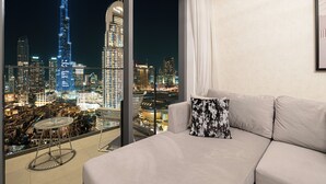 A modern living room with a large window offering a nighttime cityscape view, including a prominent skyscraper. - Fabulous Burj Khalifa Views - 5min walk to Dubai Mall (Dubai)
