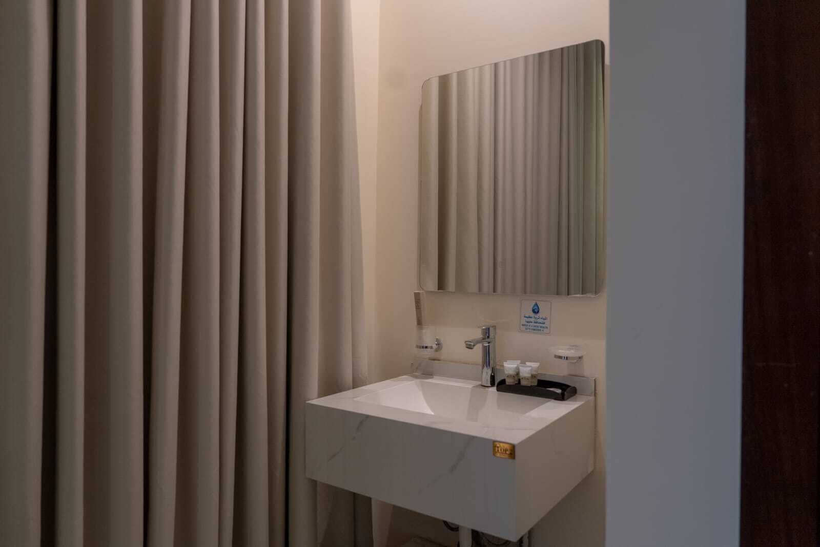 Un baño con lavamanos blanco, un espejo y un perchero para toallas.