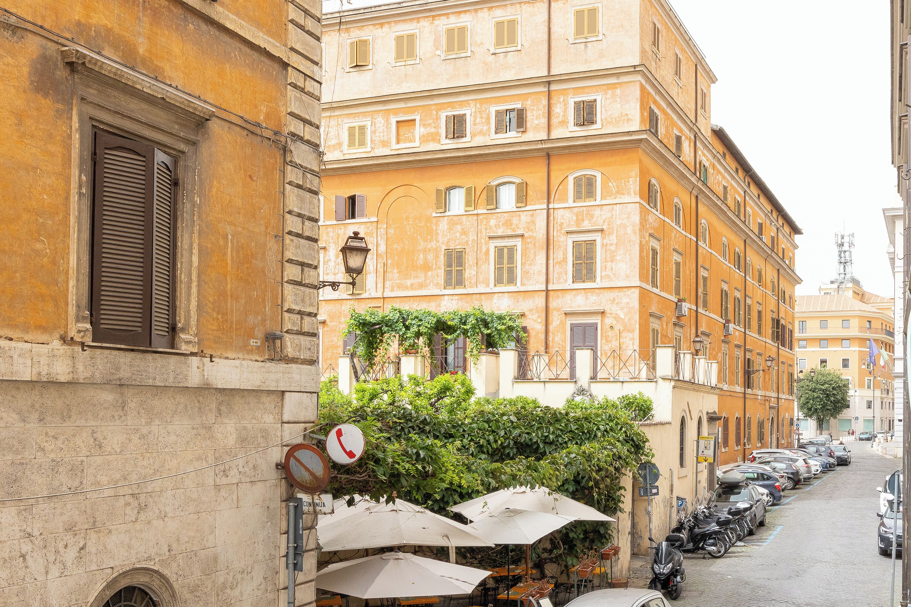 A street with parked cars and a row of outdoor tables with umbrellas.