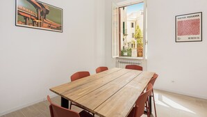 A dining area with a wooden table and red chairs, a window with a view of buildings, and two framed artworks on the walls. - Rental in Rome Mastai Trastevere Home (Rome)