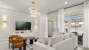A modern living room with a white sofa, a brown leather chair, a TV, and a ceiling light fixture. - 5 Bd / 4,5 Ba / Sleeps 14 / Windsor Cay Resort (Clermont)