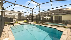 A swimming pool with a glass enclosure, surrounded by lounge chairs and a covered patio area. - 7 Bd / 6.5 Ba / Sleeps 20 / Solara Resort (Kissimmee)