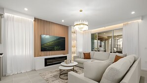 A modern living room with a large flat-screen TV, a sectional sofa, a round coffee table, and a chandelier. - 7 Bd / 6.5 Ba / Sleeps 20 / Solara Resort (Kissimmee)