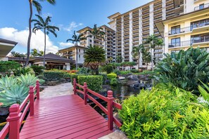 A resort with a red bridge leading to a pool area, surrounded by lush greenery and palm trees.