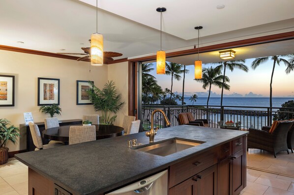 A kitchen with a large island, a dining area with chairs, and a view of the ocean at sunset. - Spacious 2BR/2BA Oceanfront Villa in Ko Olina Beach Tower with Lagoon Views (Kapolei)