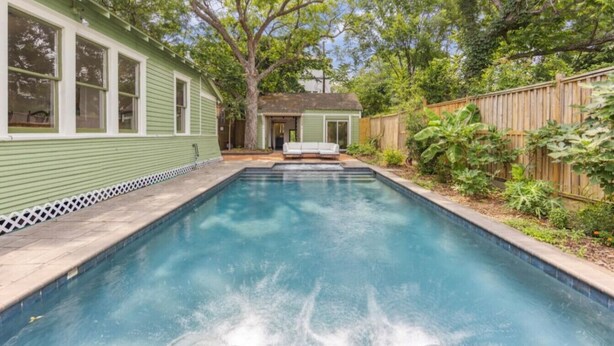 A rectangular swimming pool with a wooden deck surrounding it, a small shed in the background, and a wooden fence on the right. - Pecan Pool House  - Garden Villa #2 (Houston)