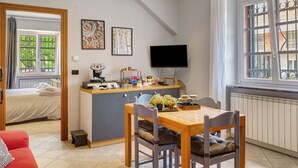 Une pièce de taille modeste comprenant un lit, une table à manger avec des chaises, un téléviseur et des œuvres d’art accrochées au mur.