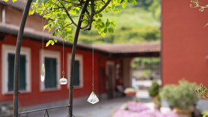 Un bâtiment à la façade rouge, un arbre orné de cristaux suspendus et un jardin où poussent des fleurs violettes.